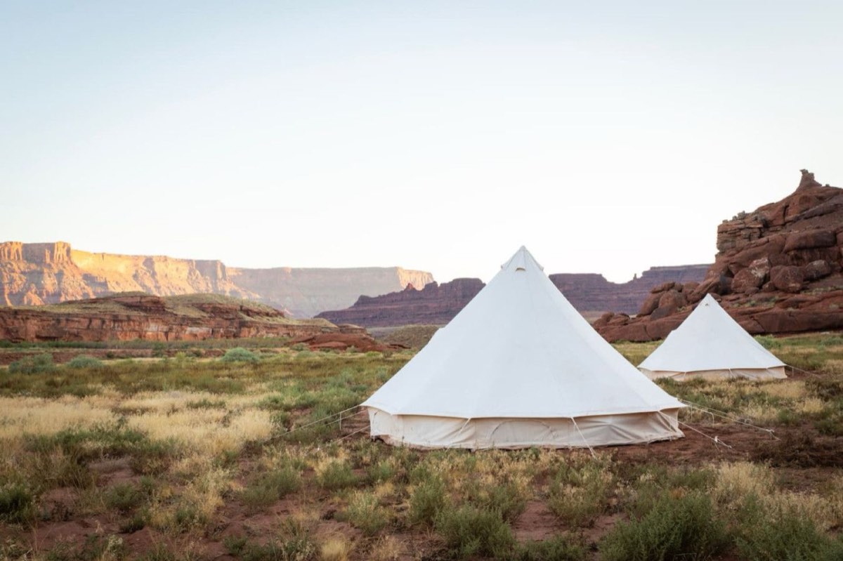 Two canvas tents on the open flat, with the mesa behind